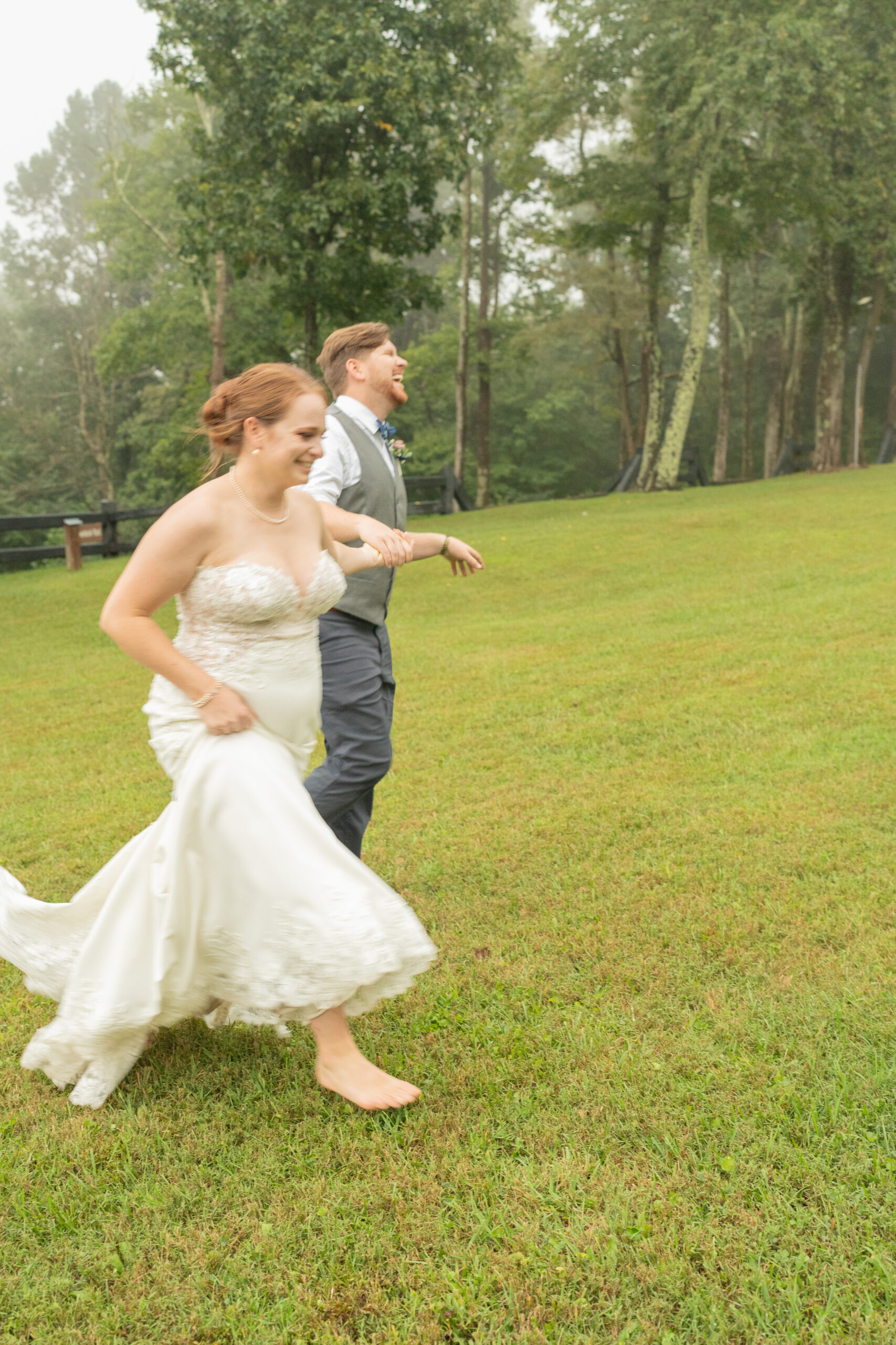 A groom leads his newbride down a hill in the mountains of Virginia. She is in her dress smiling at him.