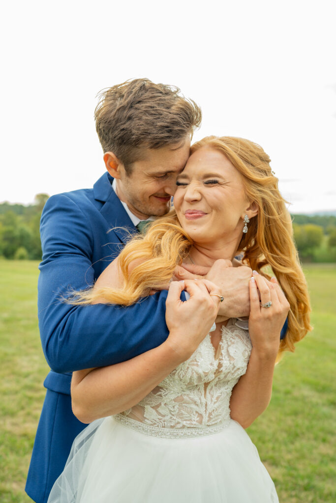 The groom hugs the bride from behind while she smiles.