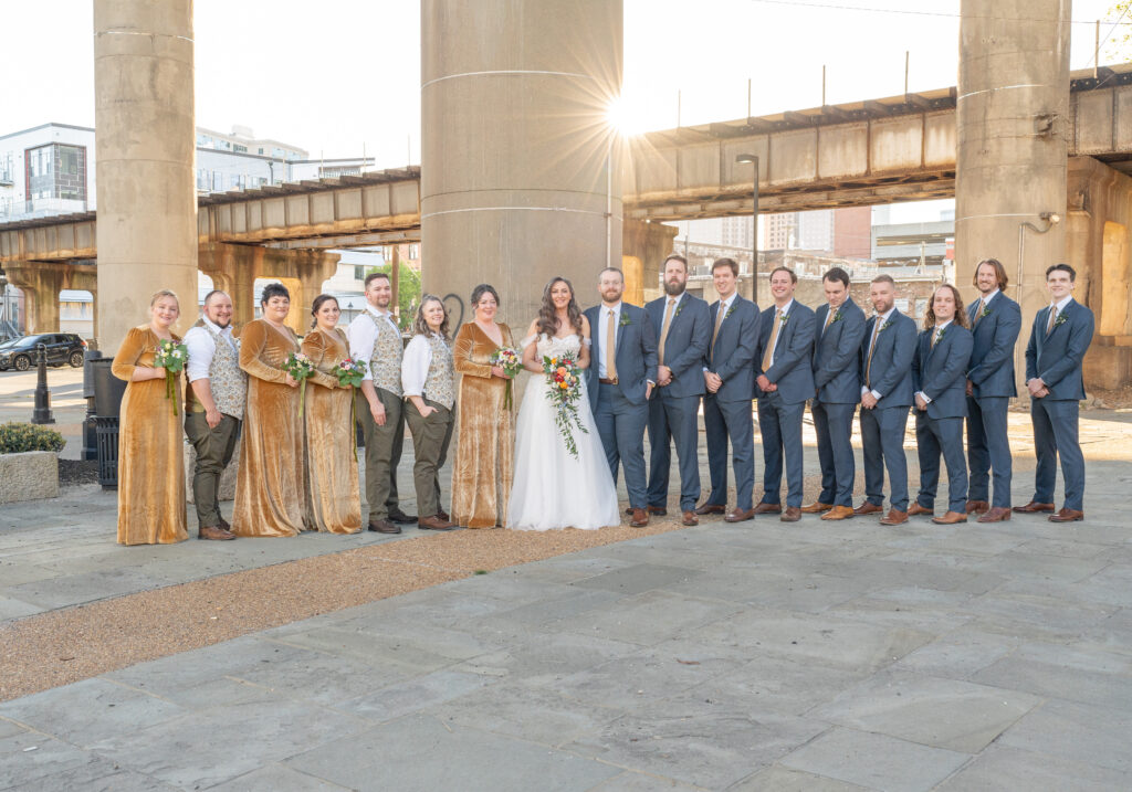 A wedding party is taking photos under an overpass in in Richmond, Va near Main Street Station. The sun is popping through the background to give a nice golden hour effect.