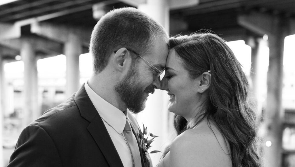 A groom and bride smile with the city of Richmond, Va behind them on their wedding day. This photo is in black and white