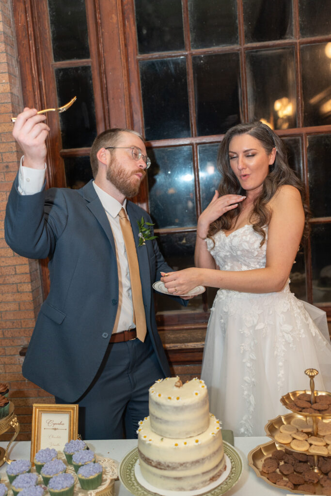 A bride and groom share their wedding cake while dancing to music in the background.