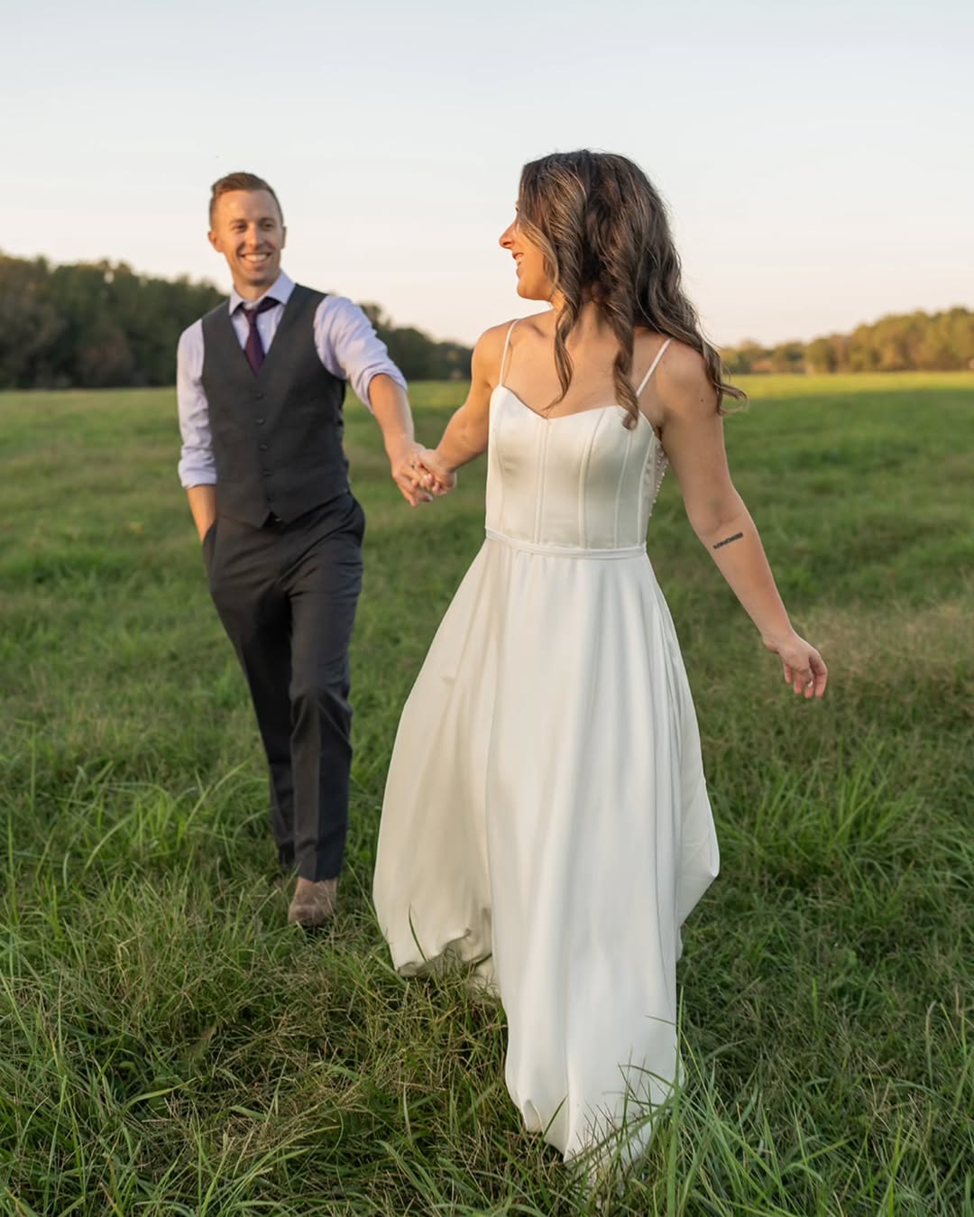 Bride and groom walking through a field near Richmond VA, captured in candid wedding photos by Mason Jesmer Photography.