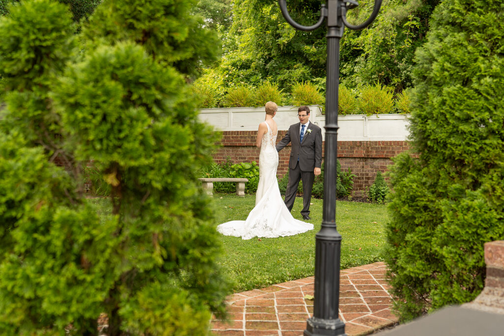 Bride and groom in the English garden at Mankin Mansion Richmond VA, framed through manicured hedges, documentary wedding photography